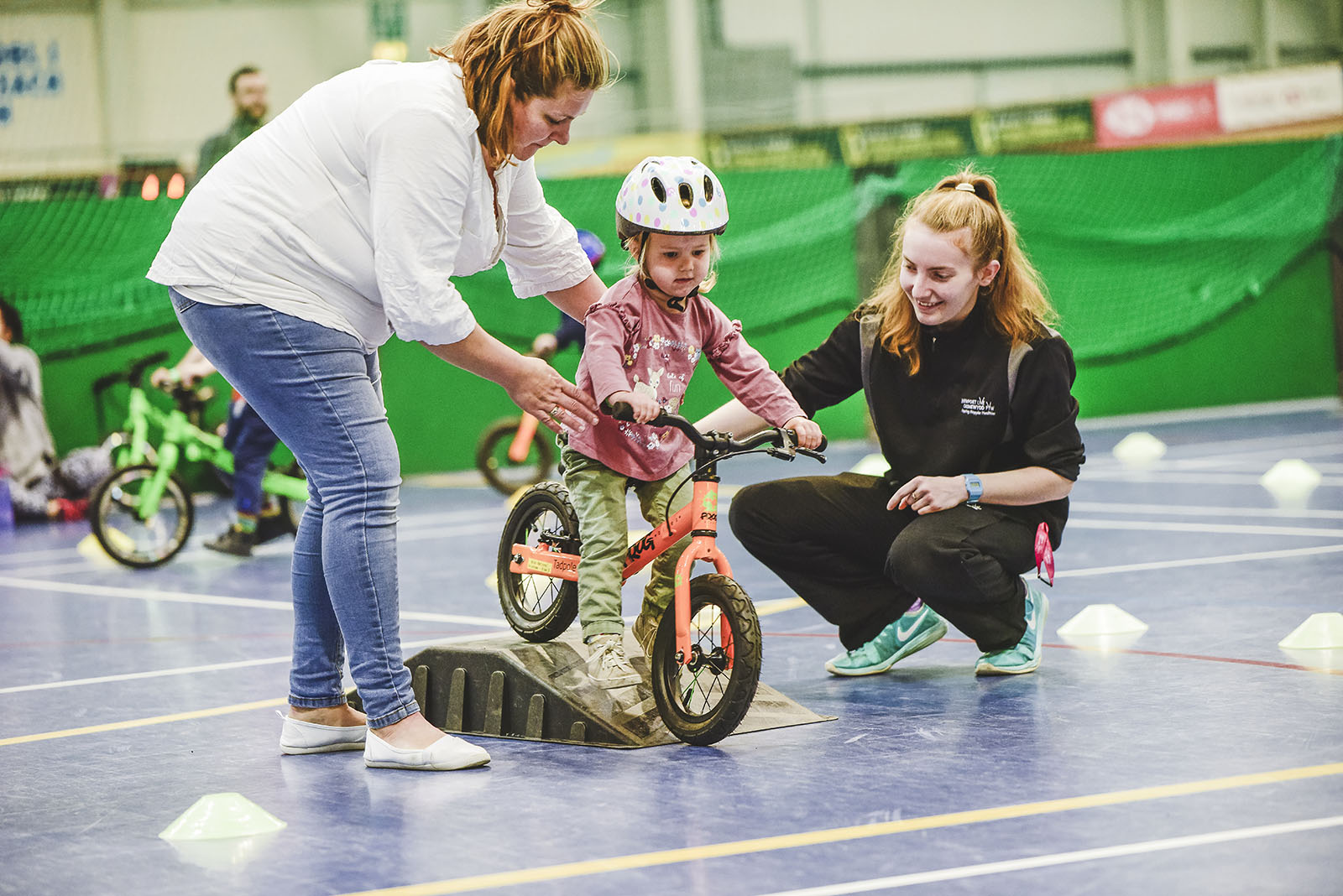 Mother and Newport Live employee helping a little girl scoot her bike over a ramp