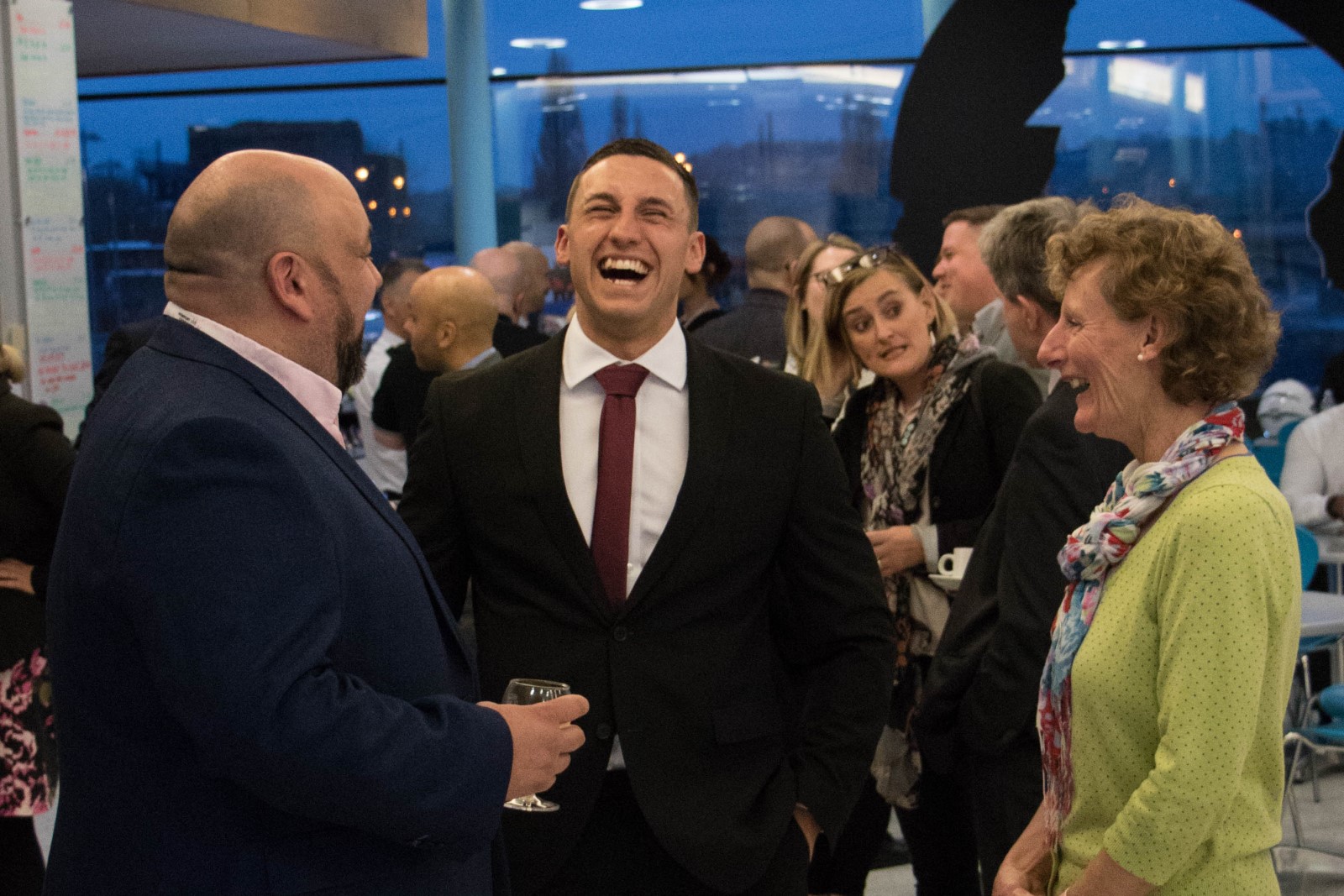 Group of people in suits stood laughing and smiling