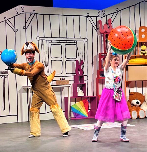 Girl and man in dog costume holding up beach balls